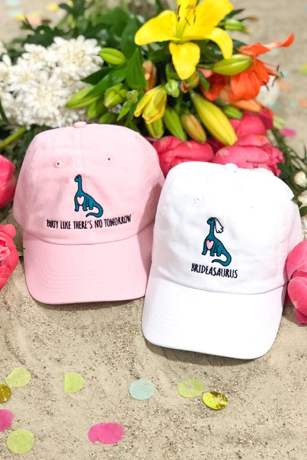 A-Roar-Able Brideasaurus Dad Hats in white and soft pink, featuring fun embroidered designs for brides.