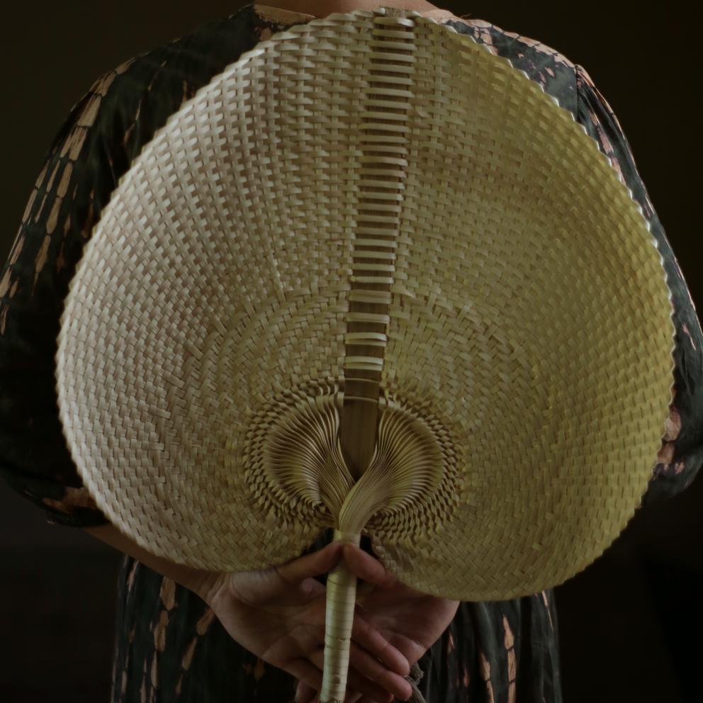 A beautifully handwoven Balinese fan made from Lontar Palm straws, showcasing intricate patterns and available in three sizes.