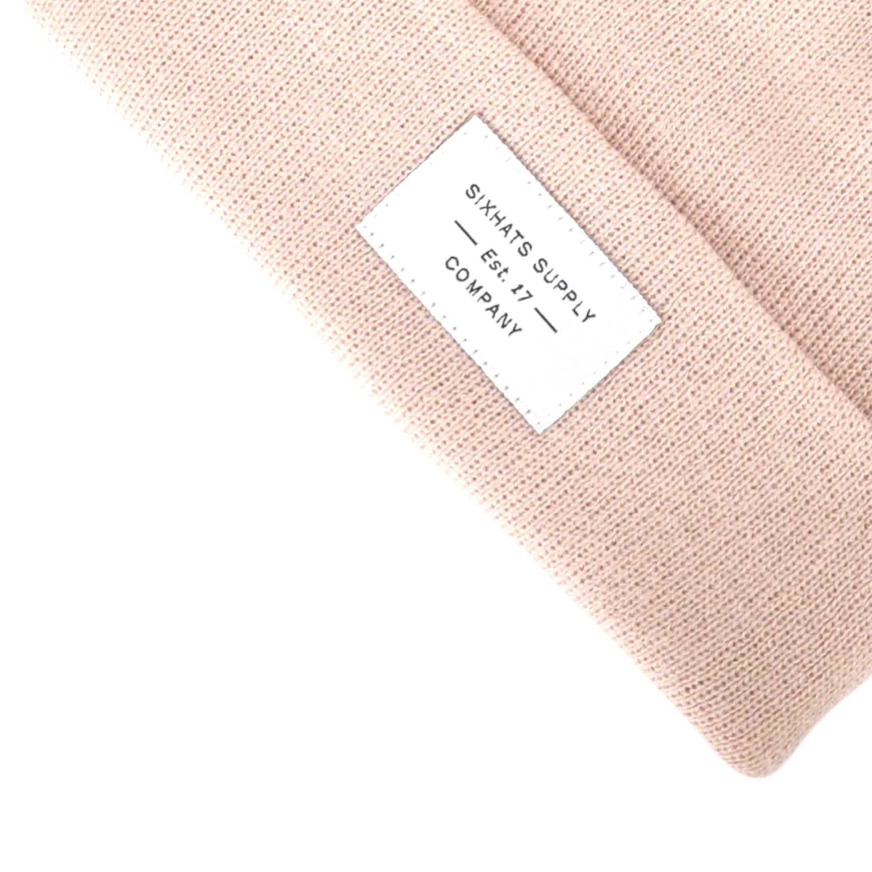 A soft beige folding beanie displayed on a neutral background, showcasing its stylish design and woven label.