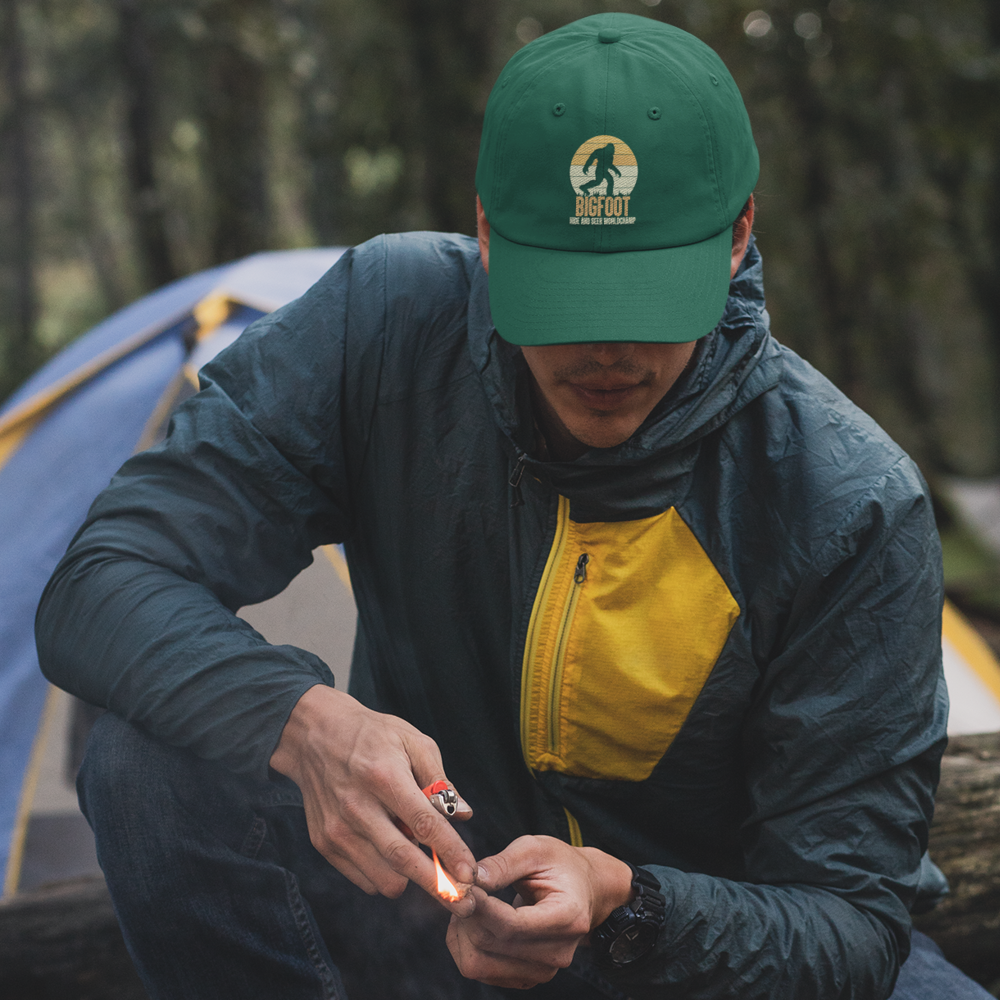 Bigfoot Hide And Seek Embroidered Baseball Hat featuring a playful design, 100% cotton material, and a comfortable snapback closure.