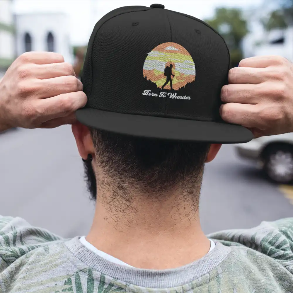 Born To Wander Embroidered Flat Bill Cap featuring a structured design, green under visor, and snapback closure, perfect for outdoor adventures.