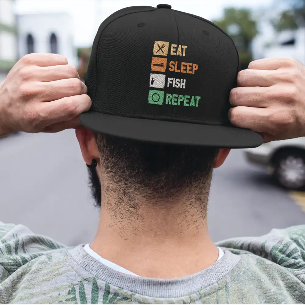 Eat Sleep Fishing Repeat Printed Flat Bill Cap featuring a stylish flat bill and fishing-themed print, made from 100% cotton with a snapback closure.