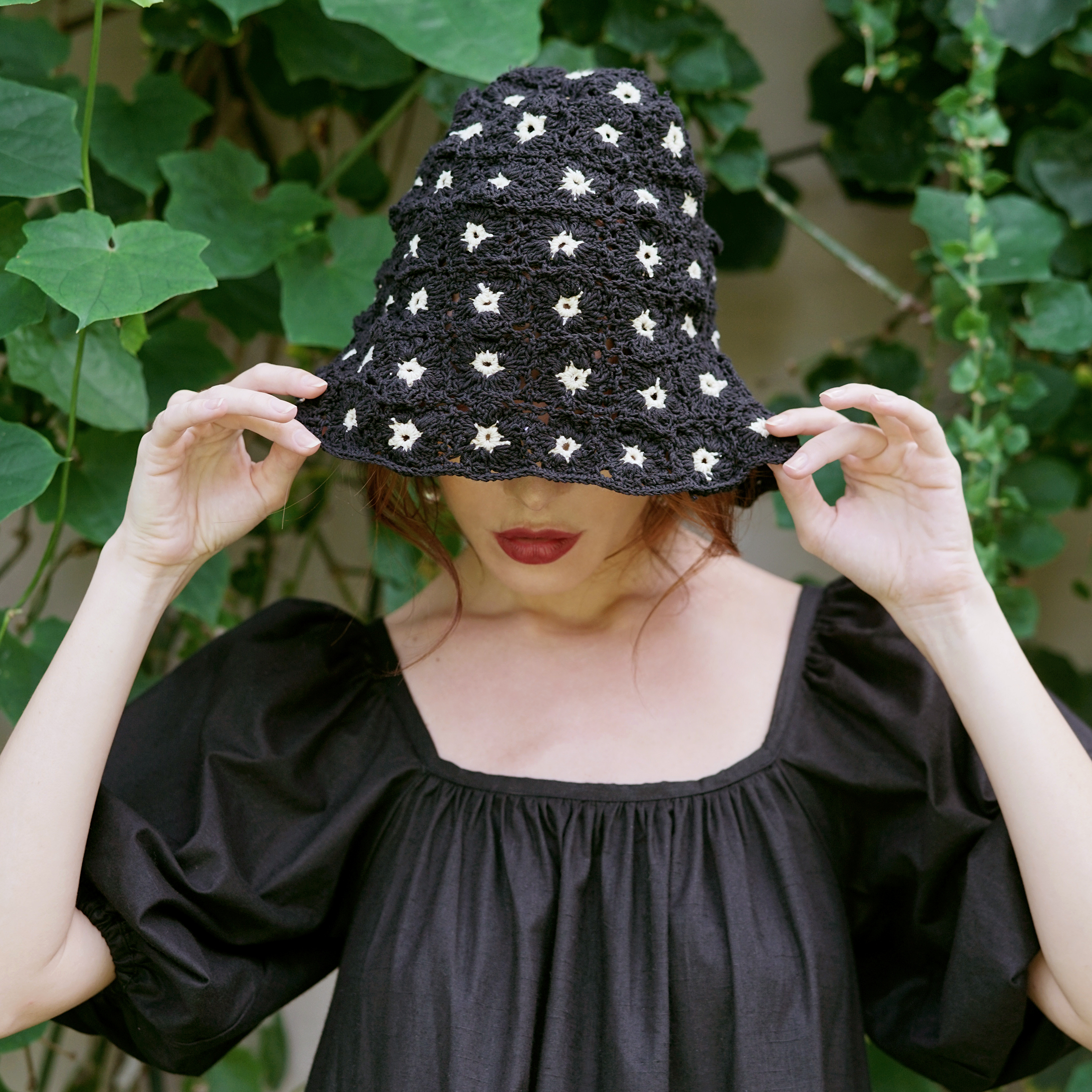 FLORA Crochet Hat in Black featuring a beautiful flower pattern, handcrafted from 100% cotton yarn, perfect for sunny outdoor occasions.