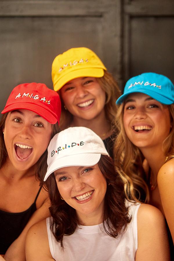 A stylish white hat labeled 'Bride' alongside colorful hats labeled 'Amigas', perfect for bachelorette parties.