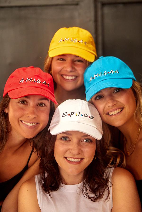 A stylish white hat labeled 'Bride' alongside colorful hats labeled 'Amigas', perfect for bachelorette parties.