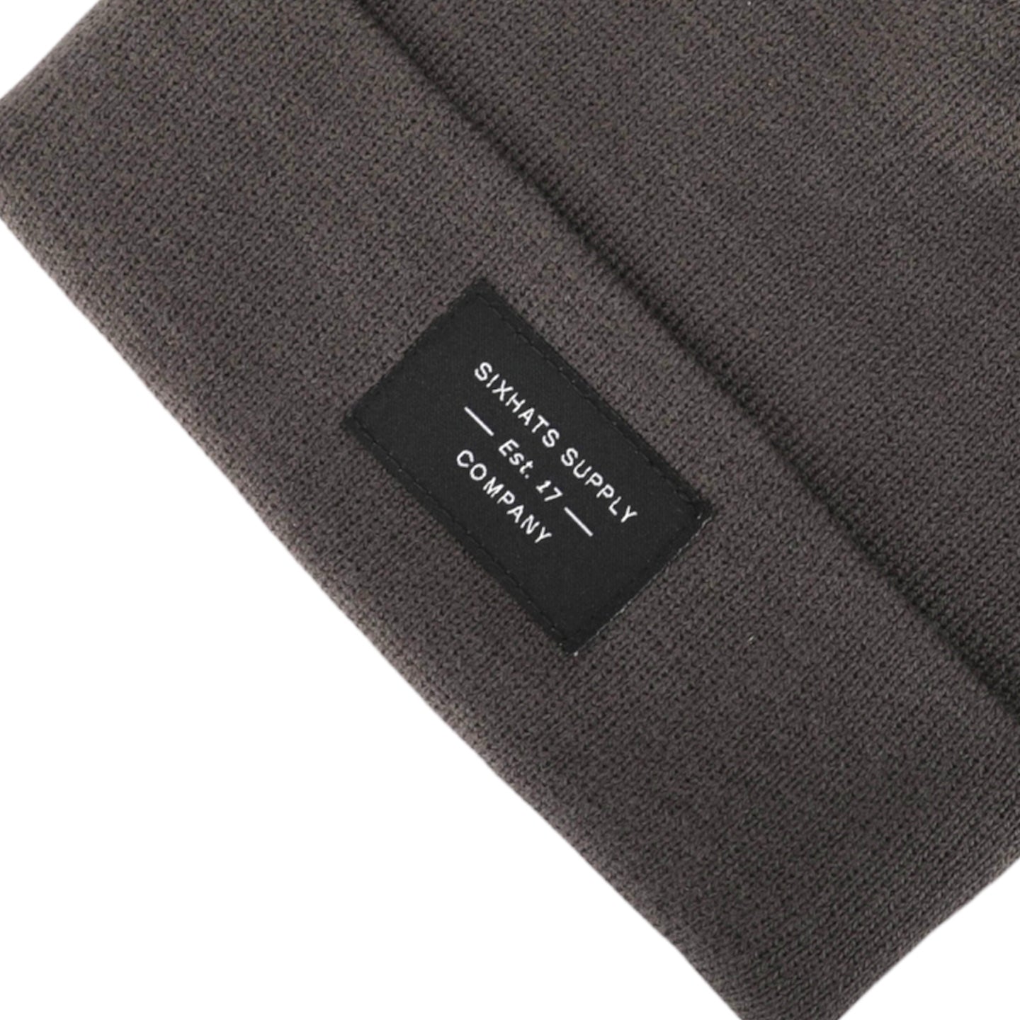 A soft grey folding beanie displayed on a wooden surface, showcasing its stylish design and classic black woven label.