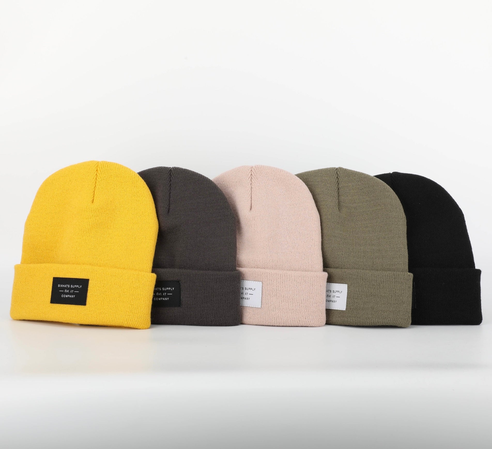 A soft grey folding beanie displayed on a wooden surface, showcasing its stylish design and classic black woven label.