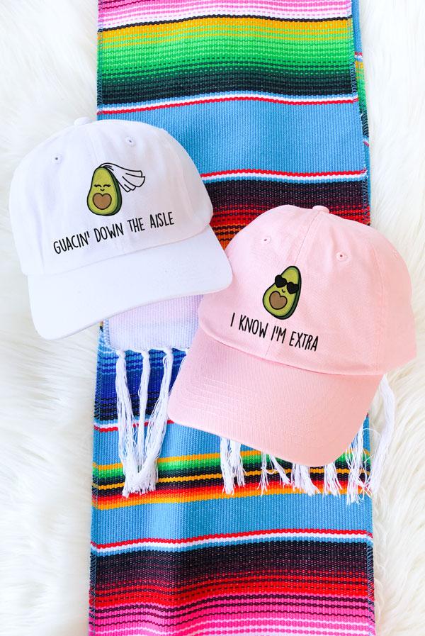 A collection of colorful fiesta avocado hats with fun phrases for weddings and celebrations, showcasing a white and soft pink design.