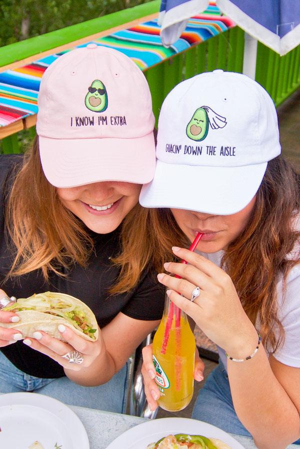 A collection of colorful fiesta avocado hats with fun phrases for weddings and celebrations, showcasing a white and soft pink design.