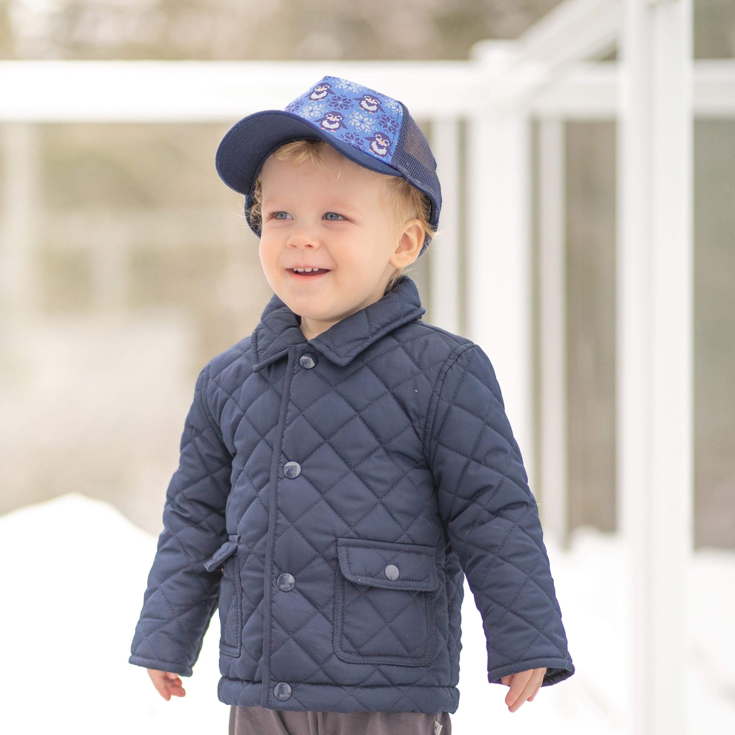 Toddler-sized trucker hat featuring a cozy penguin sweater design with a dark blue visor and mesh.