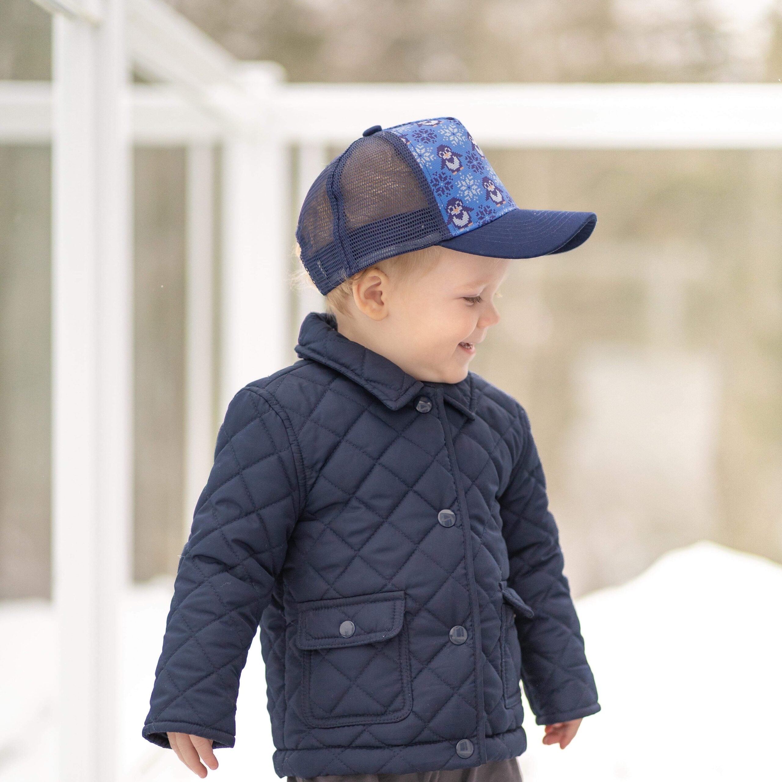 Toddler-sized trucker hat featuring a cozy penguin sweater design with a dark blue visor and mesh.