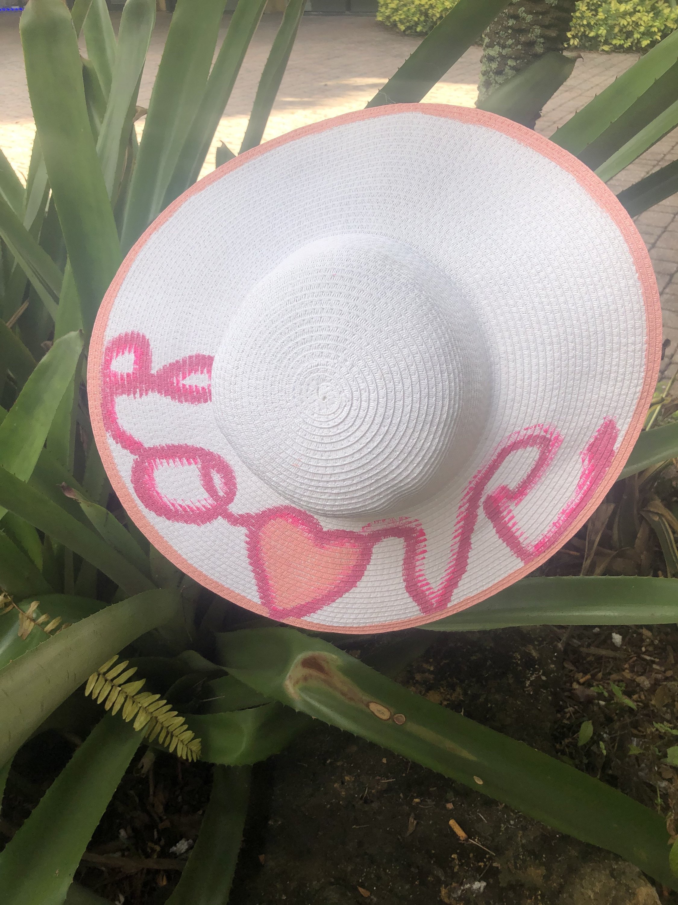 A vibrant pink handpainted sun hat with artistic designs, perfect for summer outings.