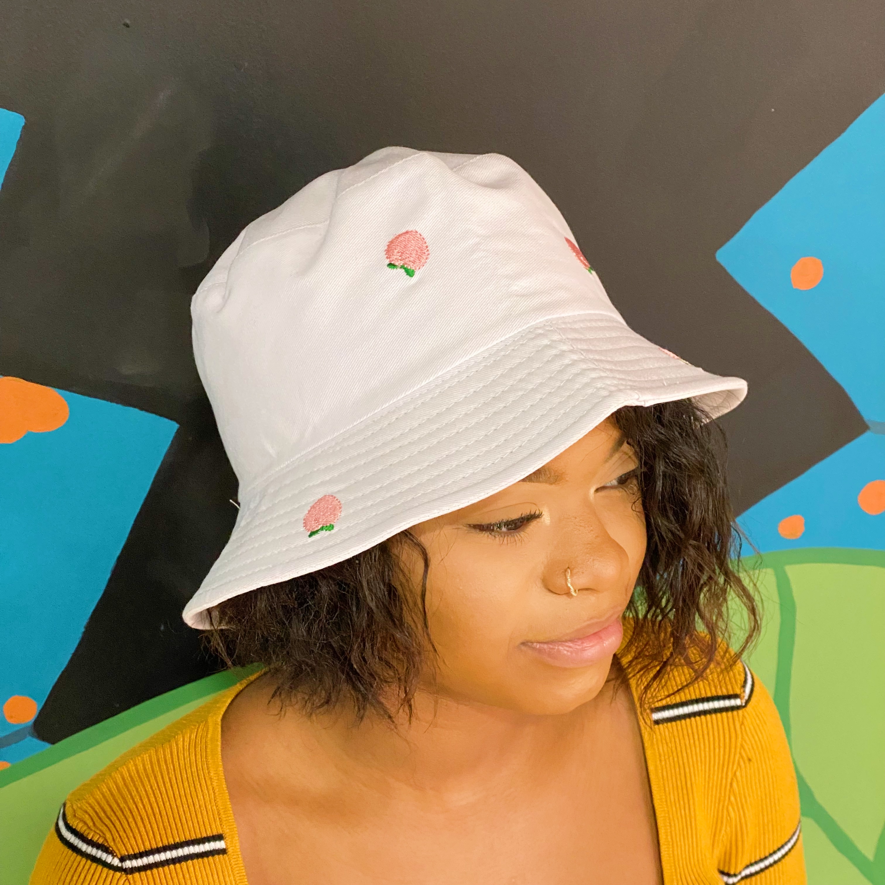 A colorful bucket hat with embroidered fruit patterns, made of high-quality cotton, perfect for sunny days.