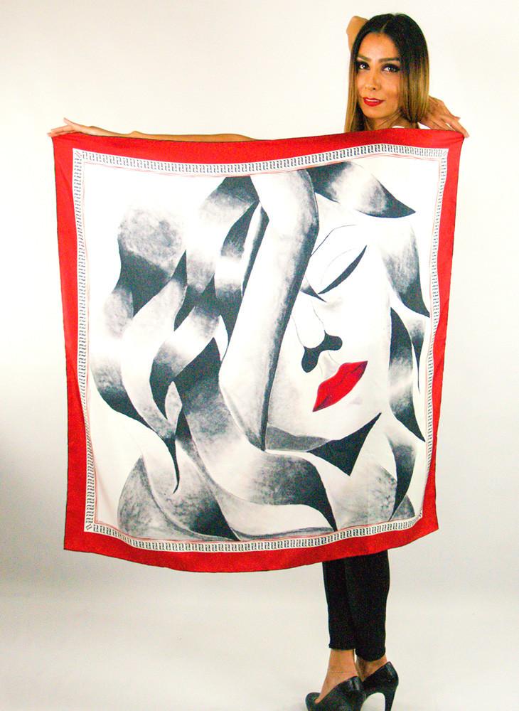 A luxurious silk scarf featuring a self-portrait design with vibrant red lips and a large closed eye, symbolizing contemplation, elegantly displayed in a gift box.