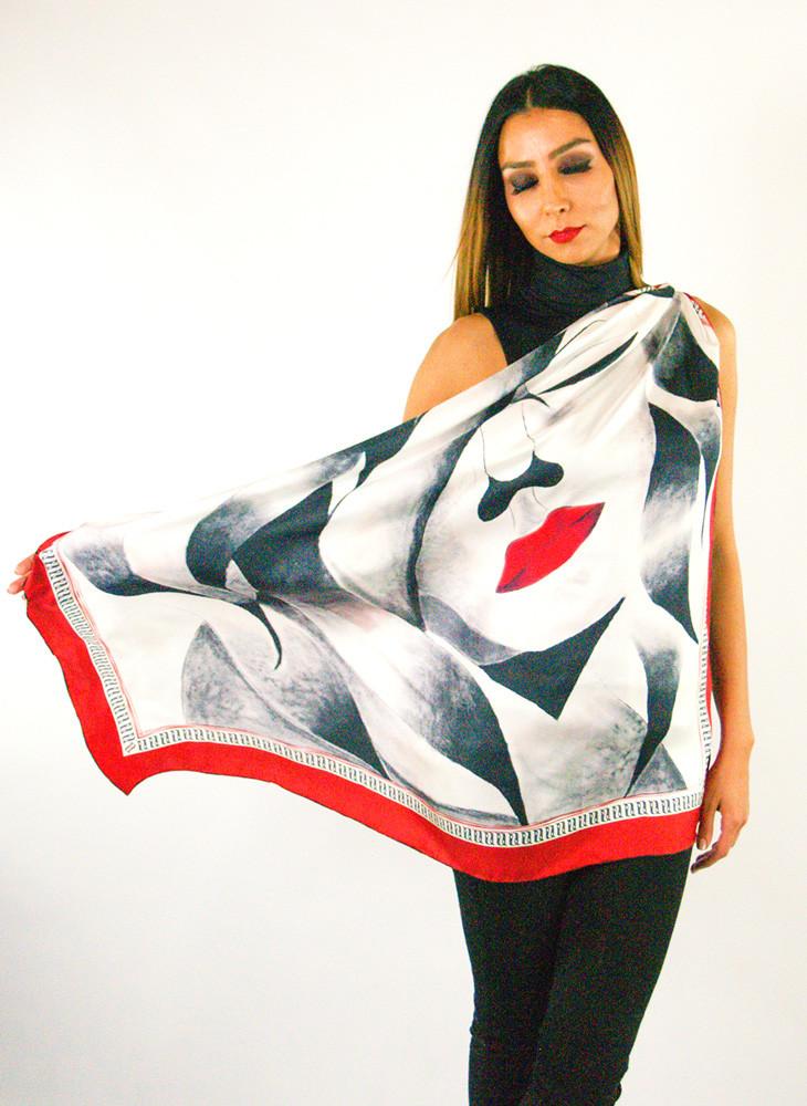 A luxurious silk scarf featuring a self-portrait design with vibrant red lips and a large closed eye, symbolizing contemplation, elegantly displayed in a gift box.