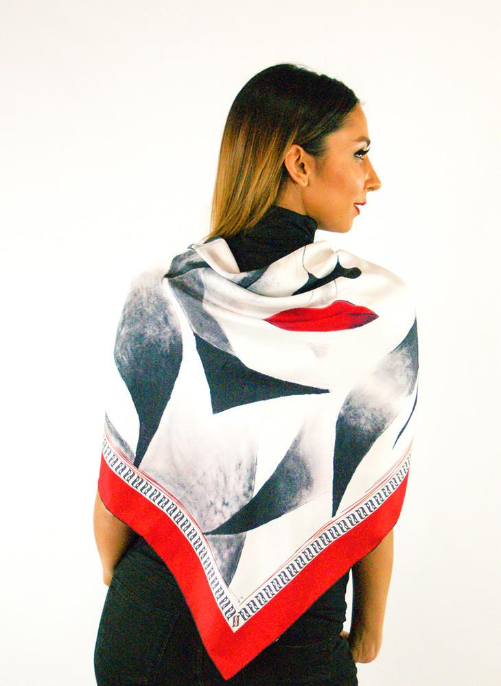 A luxurious silk scarf featuring a self-portrait design with vibrant red lips and a large closed eye, symbolizing contemplation, elegantly displayed in a gift box.