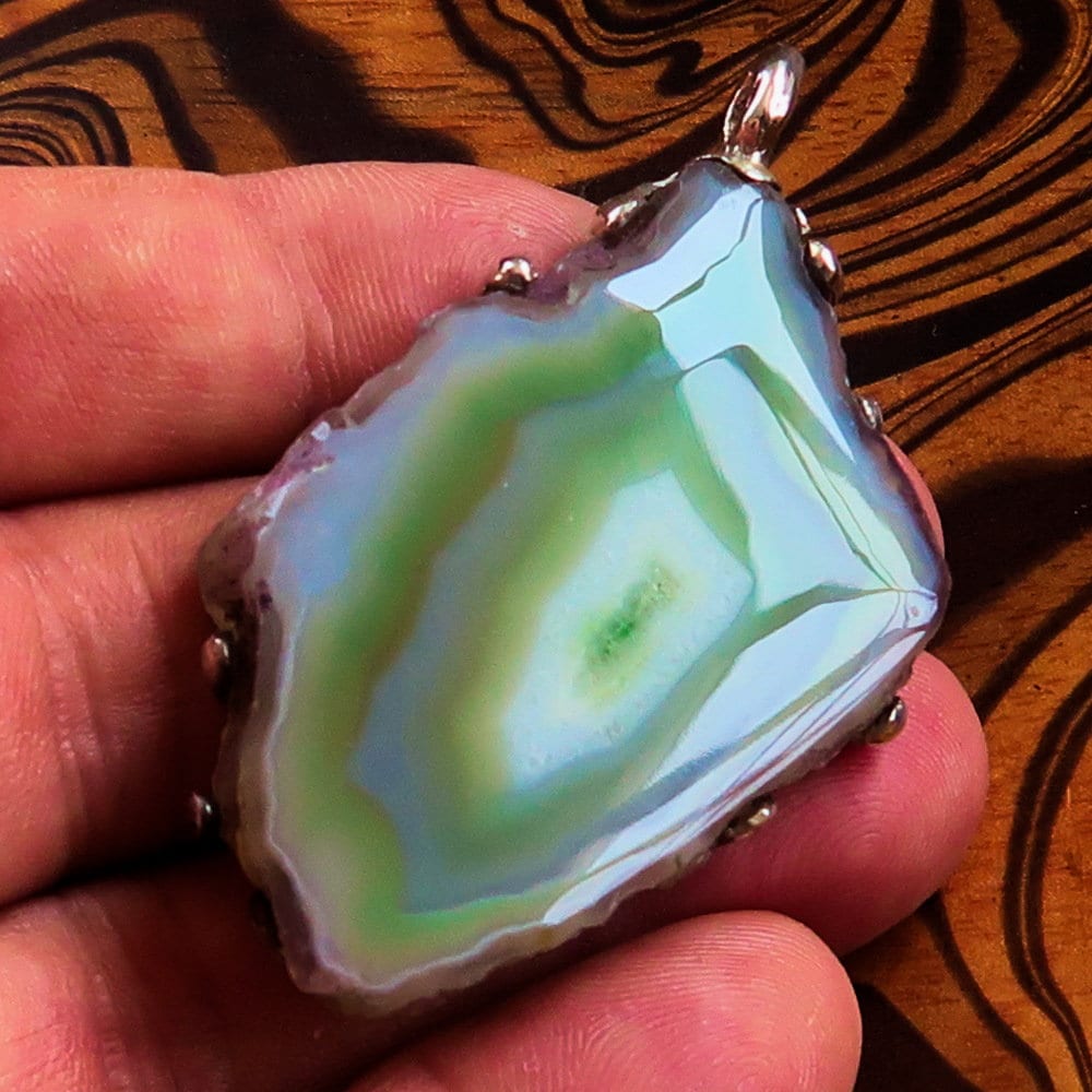 A stunning green Agate slice set in a handmade sterling silver pendant, showcasing its unique patterns and vibrant color.