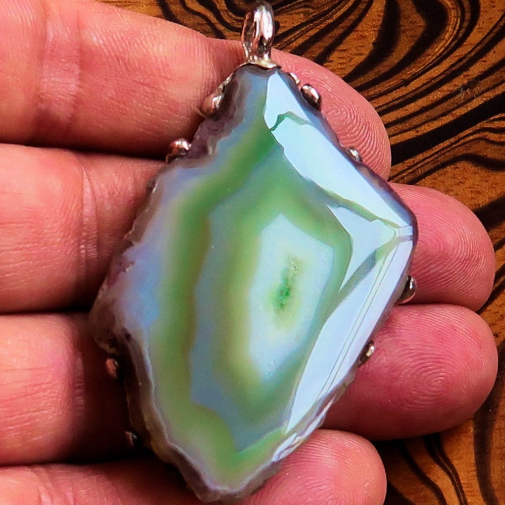 A stunning green Agate slice set in a handmade sterling silver pendant, showcasing its unique patterns and vibrant color.