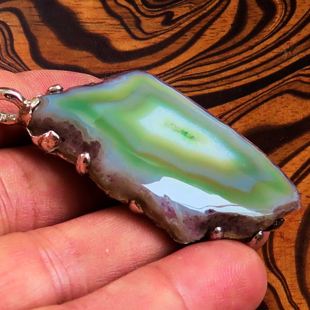 A stunning green Agate slice set in a handmade sterling silver pendant, showcasing its unique patterns and vibrant color.