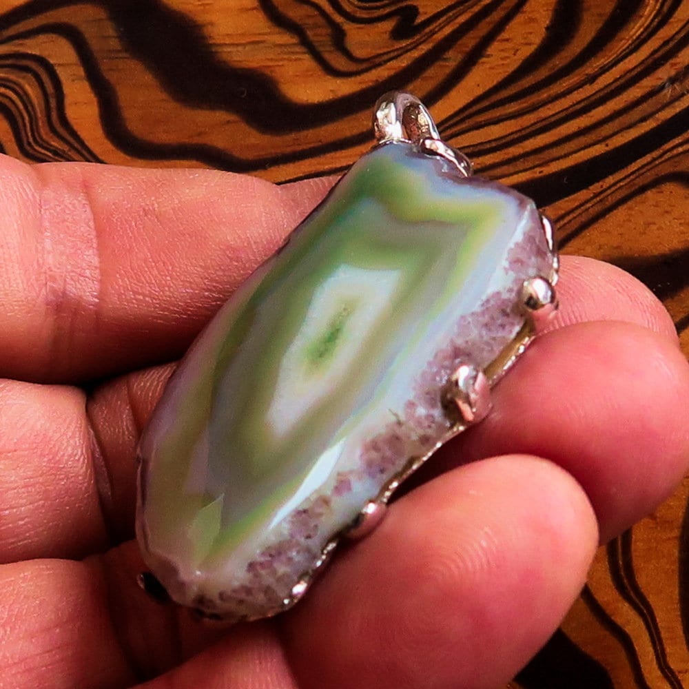 A stunning green Agate slice set in a handmade sterling silver pendant, showcasing its unique patterns and vibrant color.