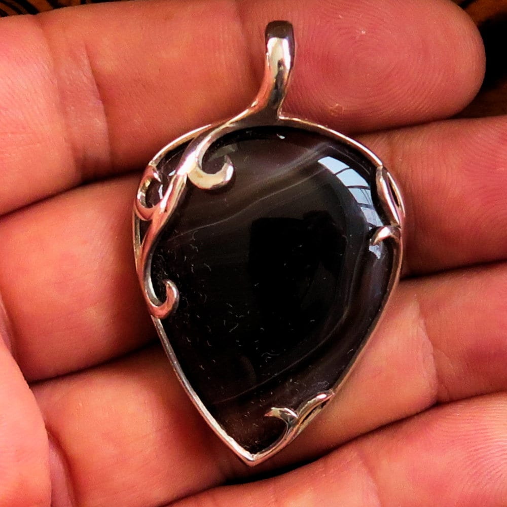 A stunning Black Agate Pendant featuring a floral design in sterling silver, showcasing a black Agate cabochon at its center.