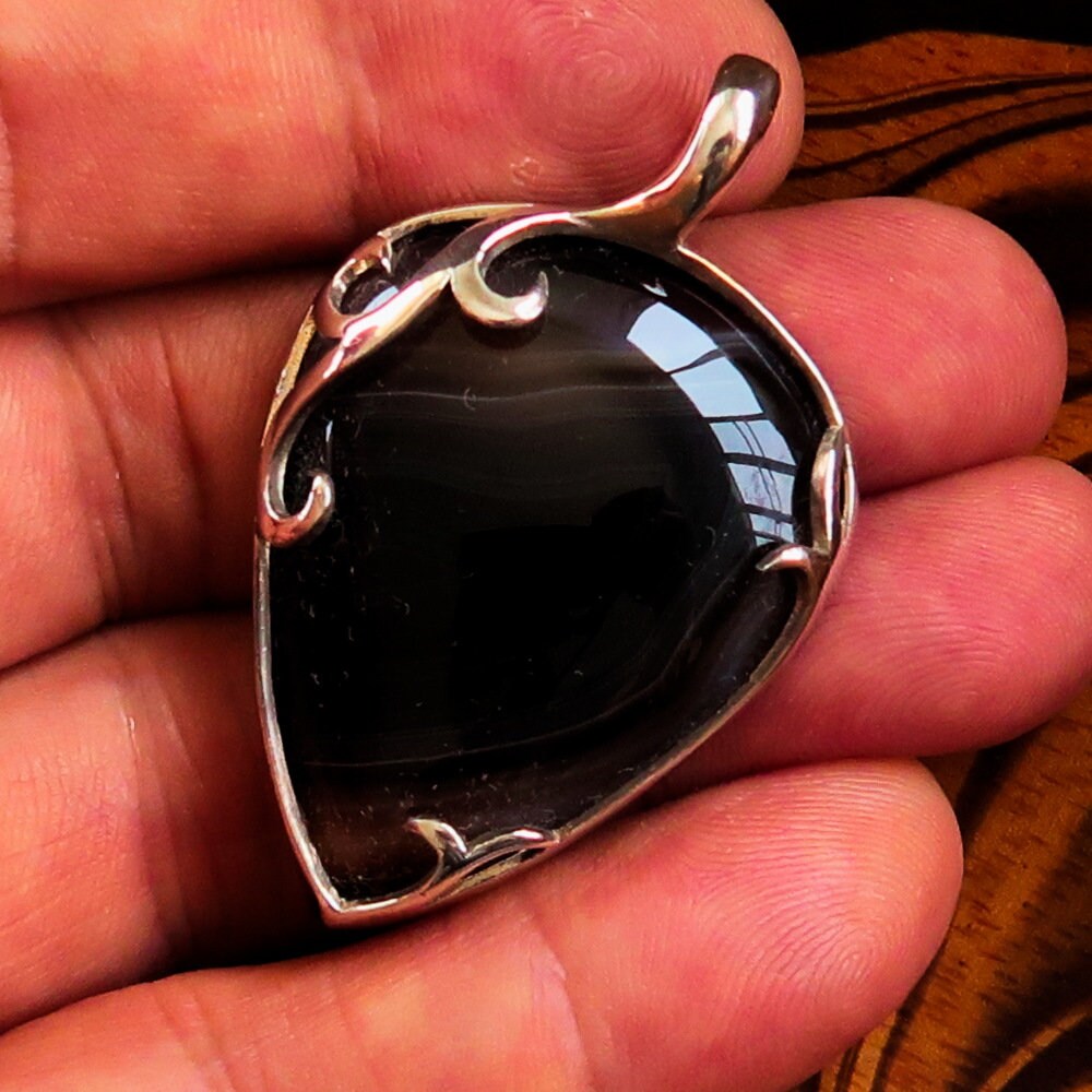 A stunning Black Agate Pendant featuring a floral design in sterling silver, showcasing a black Agate cabochon at its center.