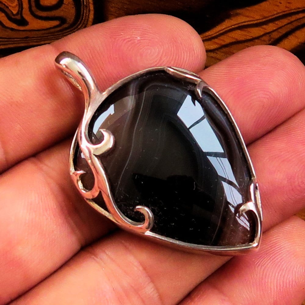 A stunning Black Agate Pendant featuring a floral design in sterling silver, showcasing a black Agate cabochon at its center.