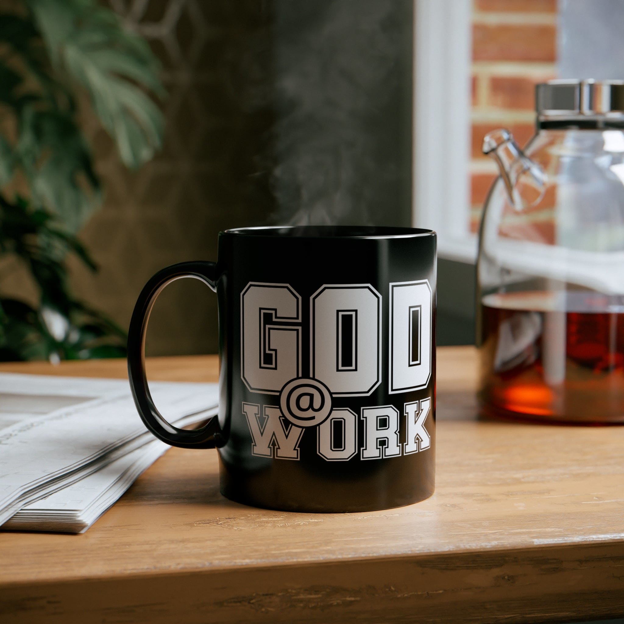 A stylish black ceramic mug with a glossy finish, featuring a white print that says 'God @ Work', perfect for coffee or tea.