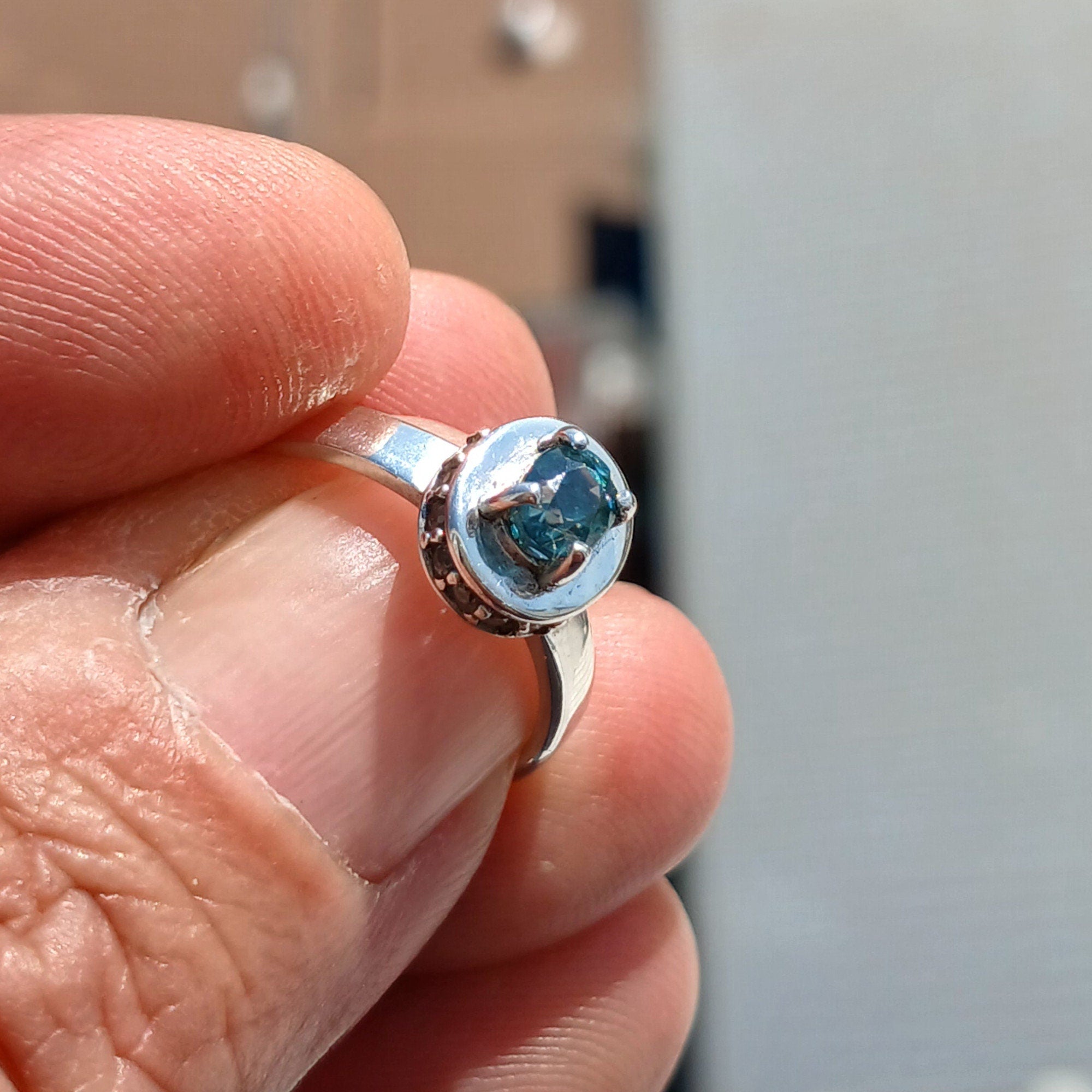 A stunning Blue Zircon Ring featuring an oval cut blue zircon centerpiece surrounded by 14 white CZ stones, set in a polished sterling silver band.