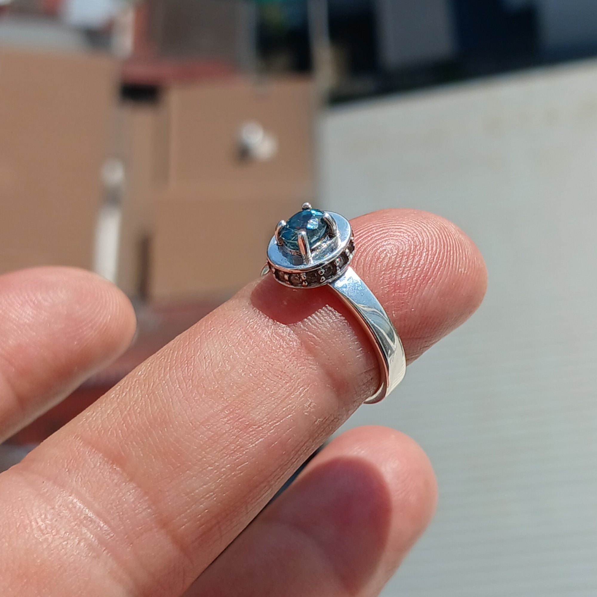 A stunning Blue Zircon Ring featuring an oval cut blue zircon centerpiece surrounded by 14 white CZ stones, set in a polished sterling silver band.