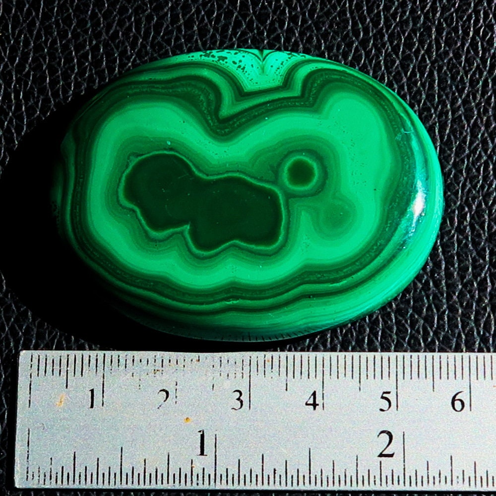 A beautiful oval-shaped Green Malachite Cabochon, showcasing vibrant green hues and unique patterns, measuring 56 mm x 42 mm.