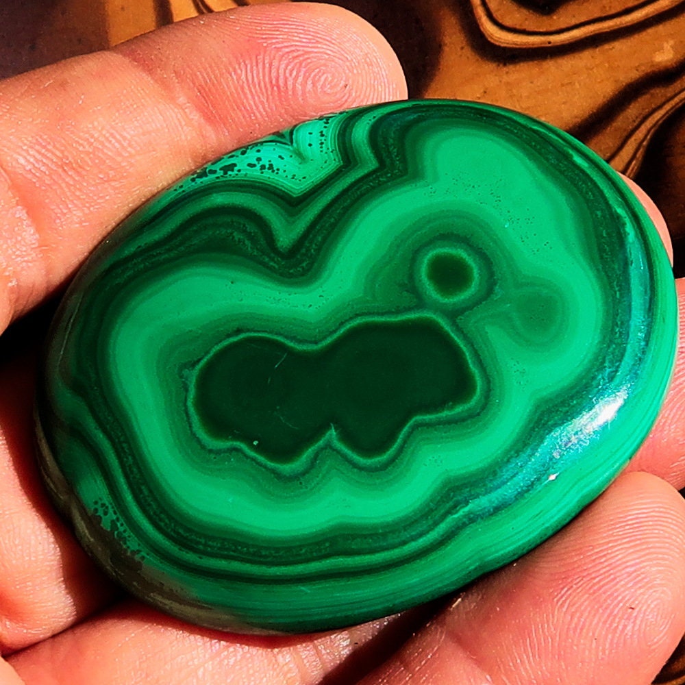 A beautiful oval-shaped Green Malachite Cabochon, showcasing vibrant green hues and unique patterns, measuring 56 mm x 42 mm.