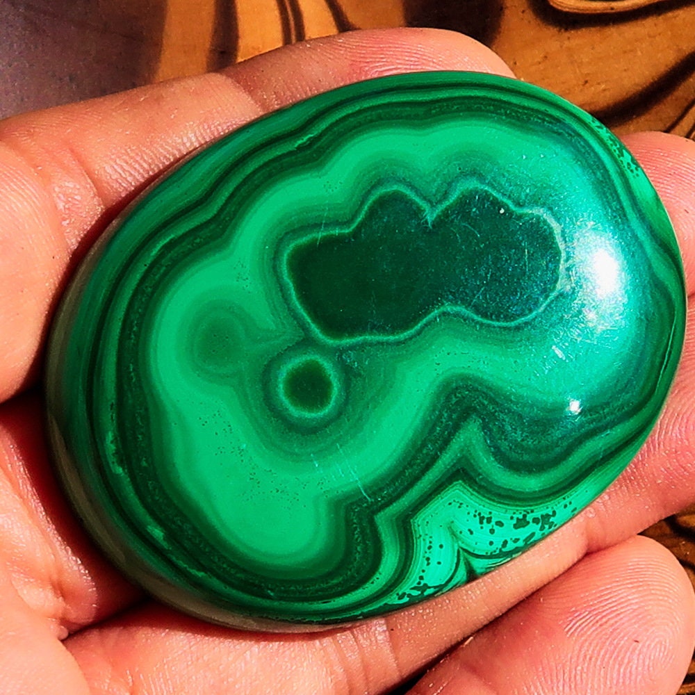 A beautiful oval-shaped Green Malachite Cabochon, showcasing vibrant green hues and unique patterns, measuring 56 mm x 42 mm.