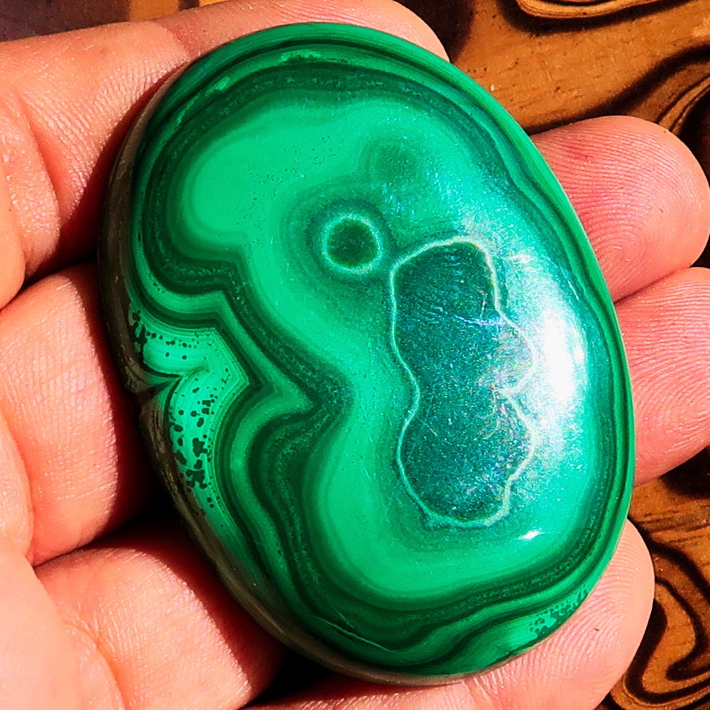 A beautiful oval-shaped Green Malachite Cabochon, showcasing vibrant green hues and unique patterns, measuring 56 mm x 42 mm.