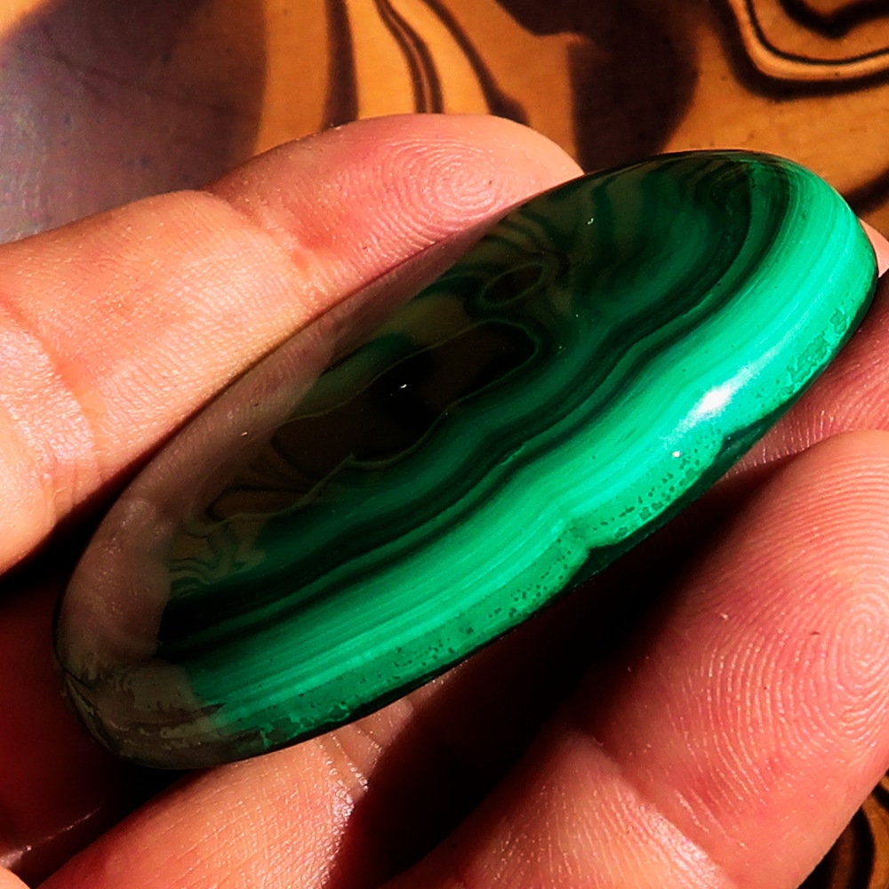 A beautiful oval-shaped Green Malachite Cabochon, showcasing vibrant green hues and unique patterns, measuring 56 mm x 42 mm.