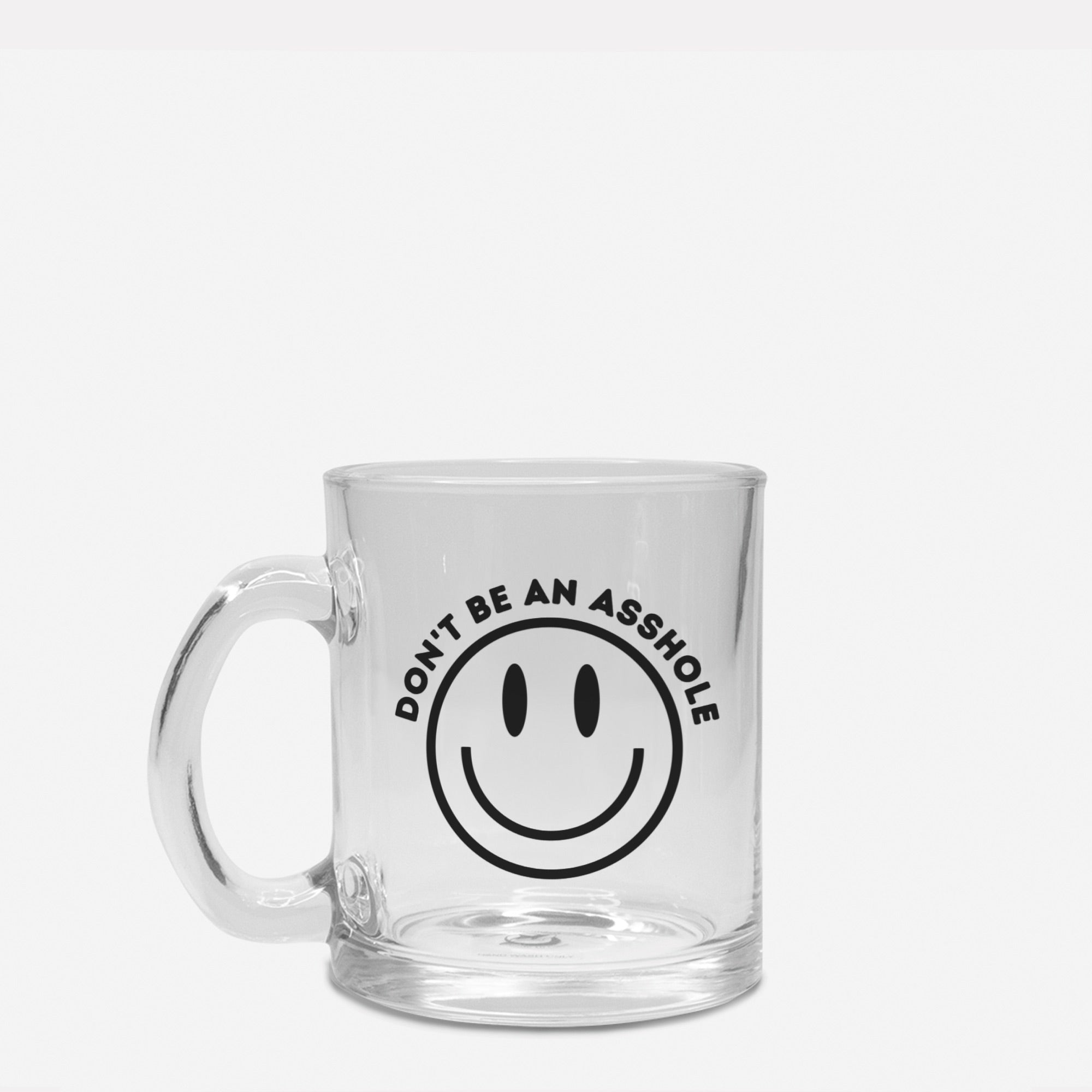 A clear glass mug with the phrase 'Don't Be An Asshole' printed on it, filled with a warm beverage.