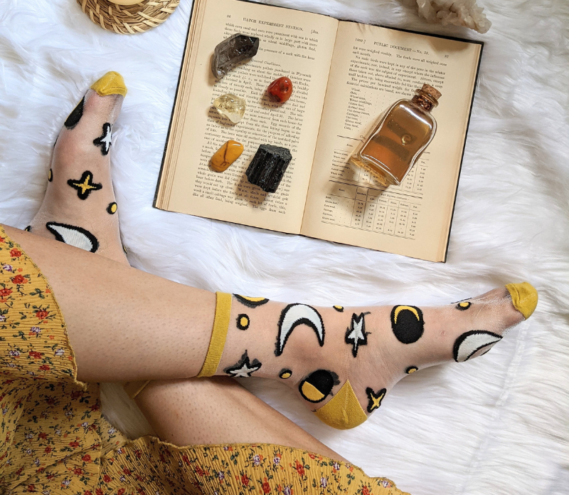 A pair of stylish embroidered mesh ankle socks featuring celestial designs with moons, stars, and botanical motifs in lavender and sunshine yellow trims.