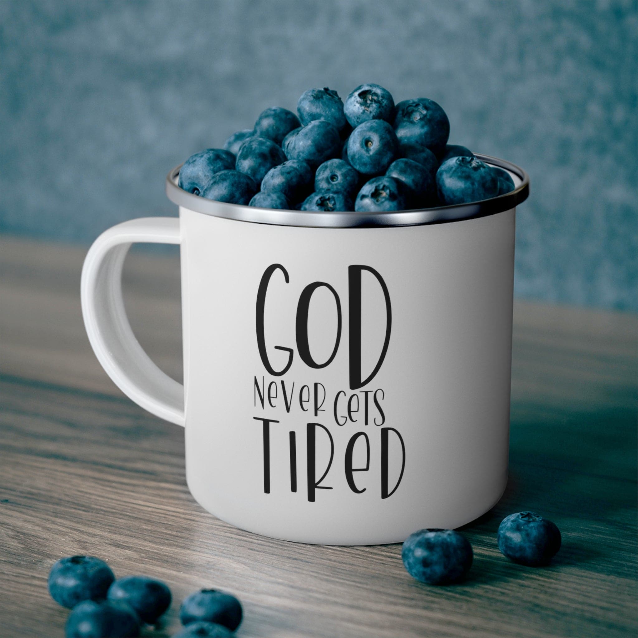 Black enamel camping mug with motivational quote 'God Never Gets Tired', featuring a C-handle and rounded corners.