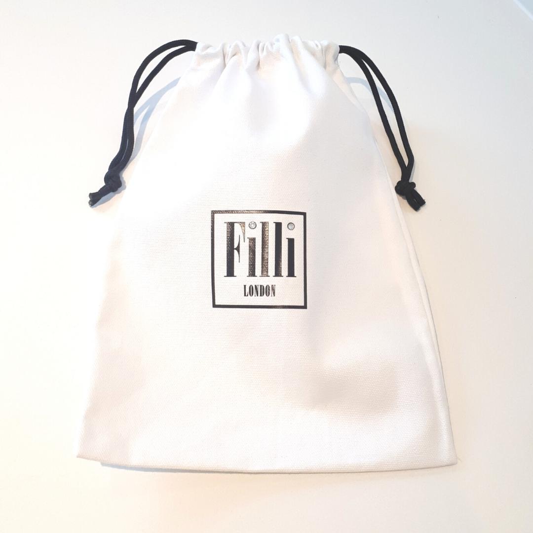 Filli London Naked Flip Flops in Black on White with embossed logo and rice pattern footbed, displayed in a cotton drawstring bag.