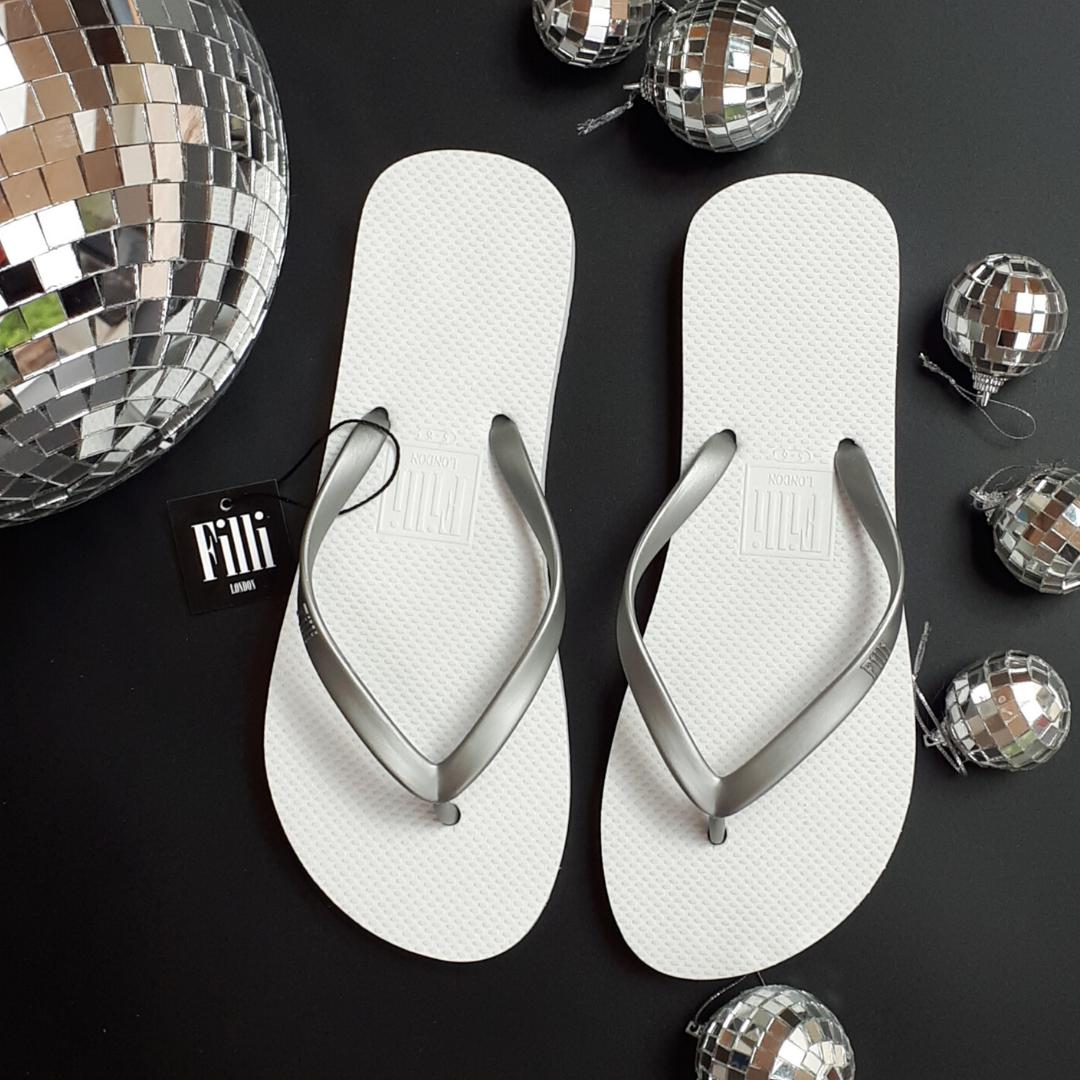 Filli London Naked Flip Flops in Silver on White with a smooth strap and rubber sole, displayed in a cotton drawstring bag.