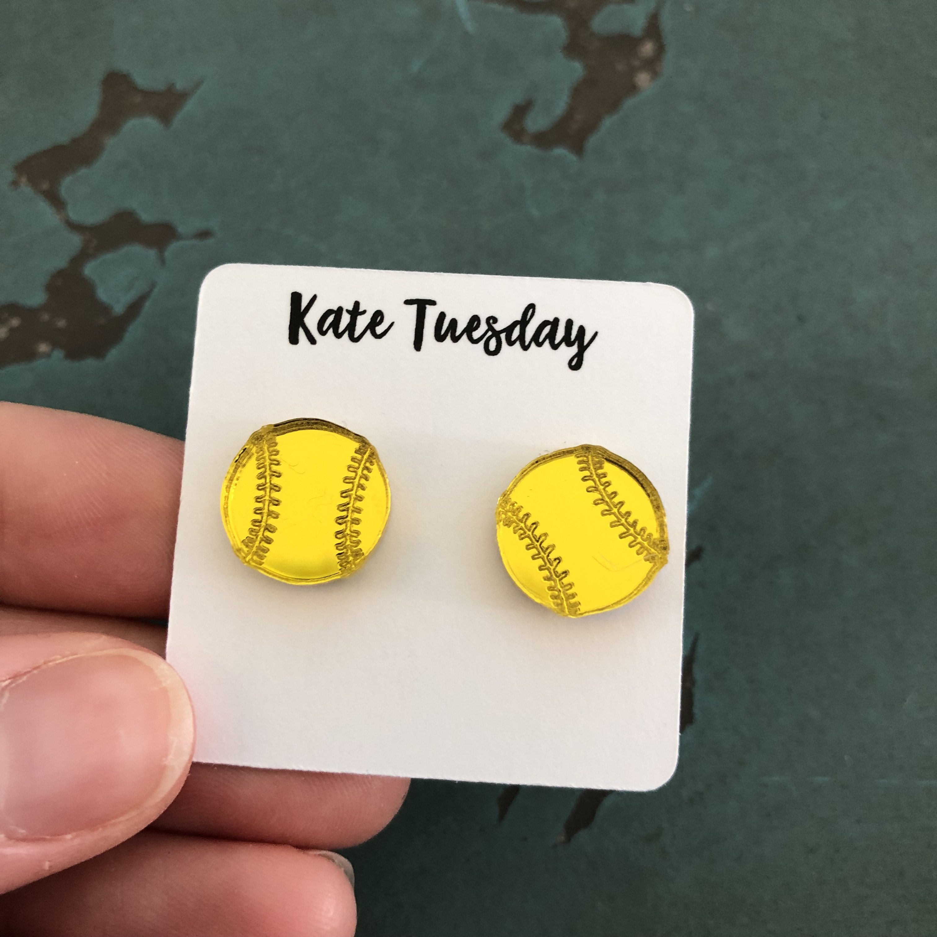 A pair of elegant gold earrings shaped like softballs, featuring a nickel and lead-free post for comfortable wear.