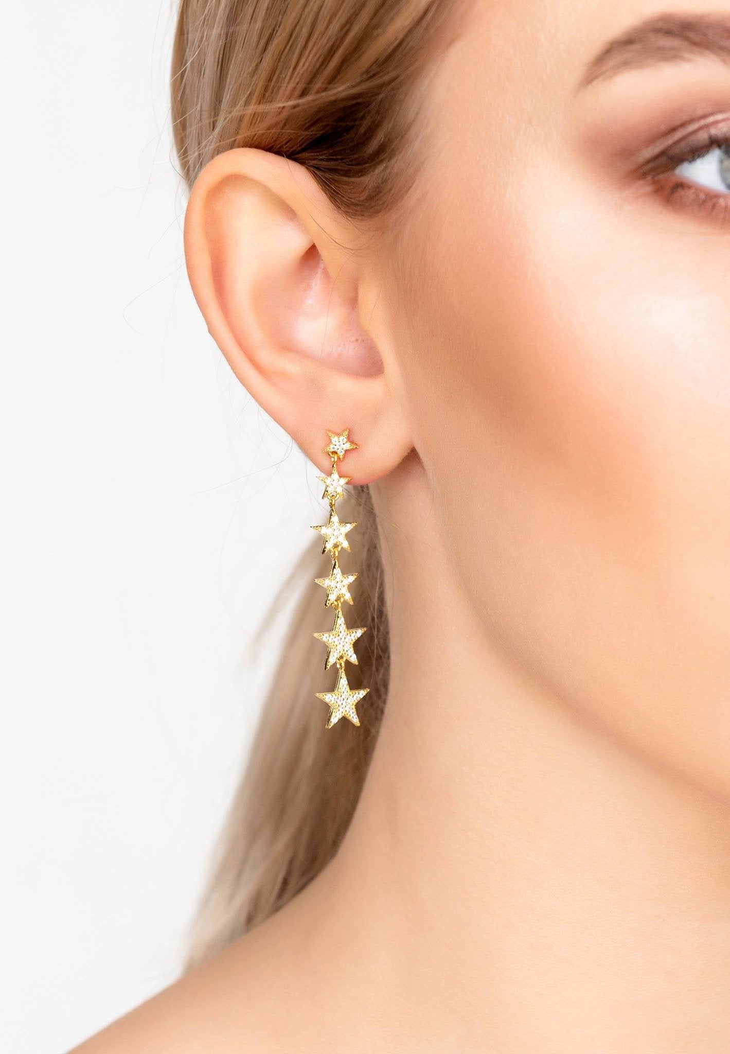 A pair of elegant graduated star drop earrings in gold, featuring six stars adorned with sparkling zircon detailing, hanging gracefully.