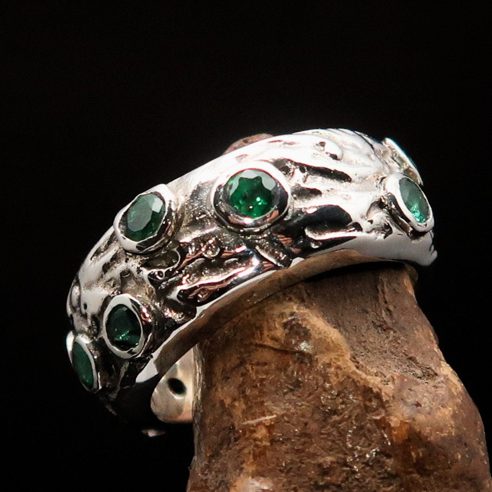 A stunning handmade green emerald ring featuring 11 irregular settings of emeralds in a polished sterling silver band.