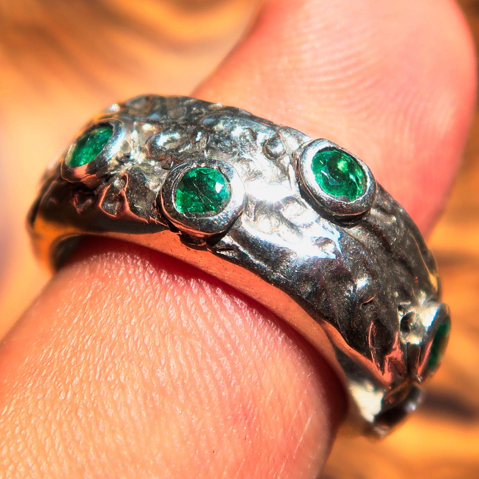 A stunning handmade green emerald ring featuring 11 irregular settings of emeralds in a polished sterling silver band.