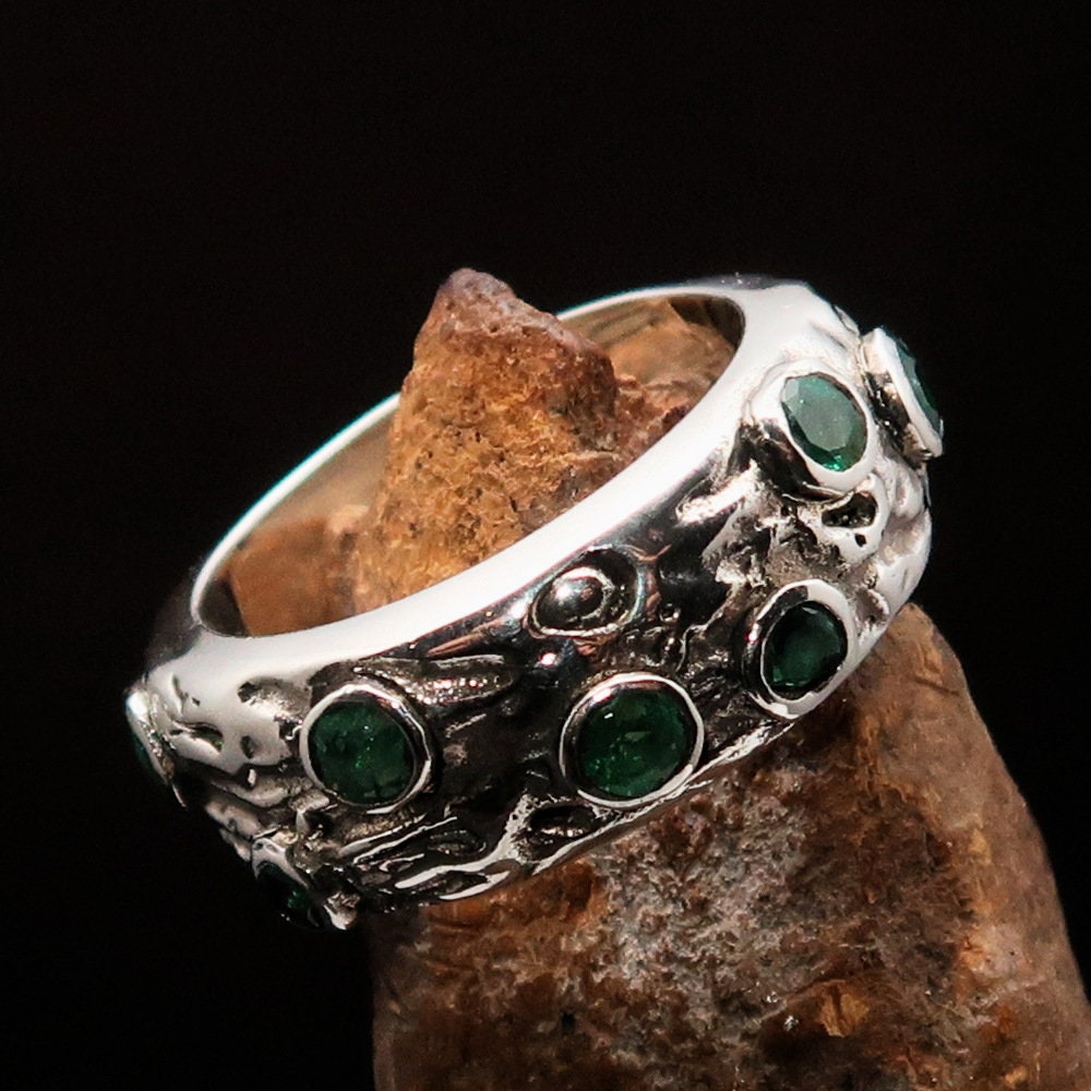 A stunning handmade green emerald ring featuring 11 irregular settings of emeralds in a polished sterling silver band.