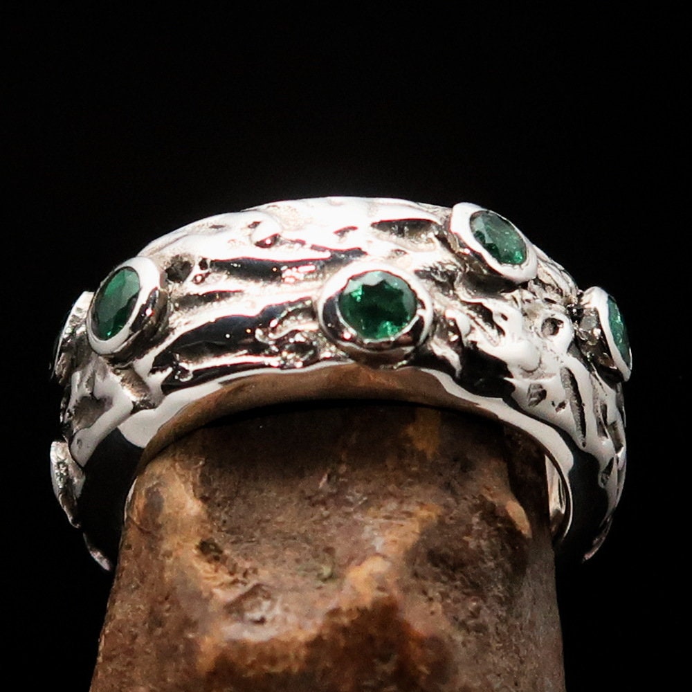 A stunning handmade green emerald ring featuring 11 irregular settings of emeralds in a polished sterling silver band.