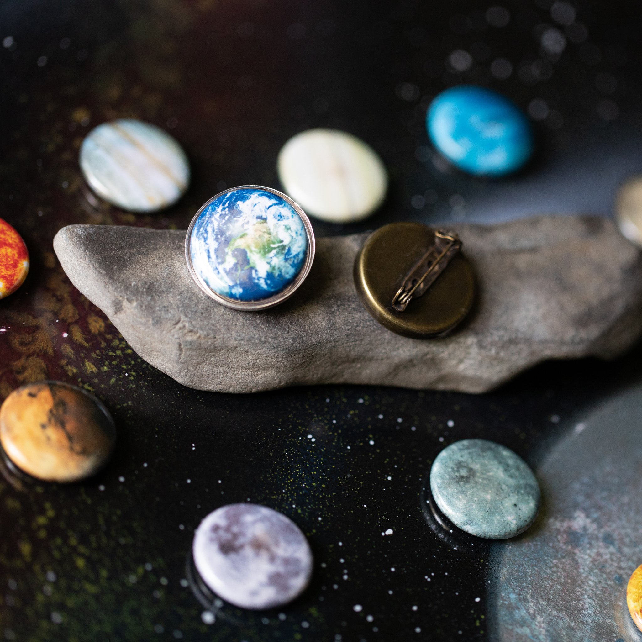 Interchangeable Solar System Lapel Pin featuring 10 images of planets, the Sun, and the Moon in silver and bronze tones.