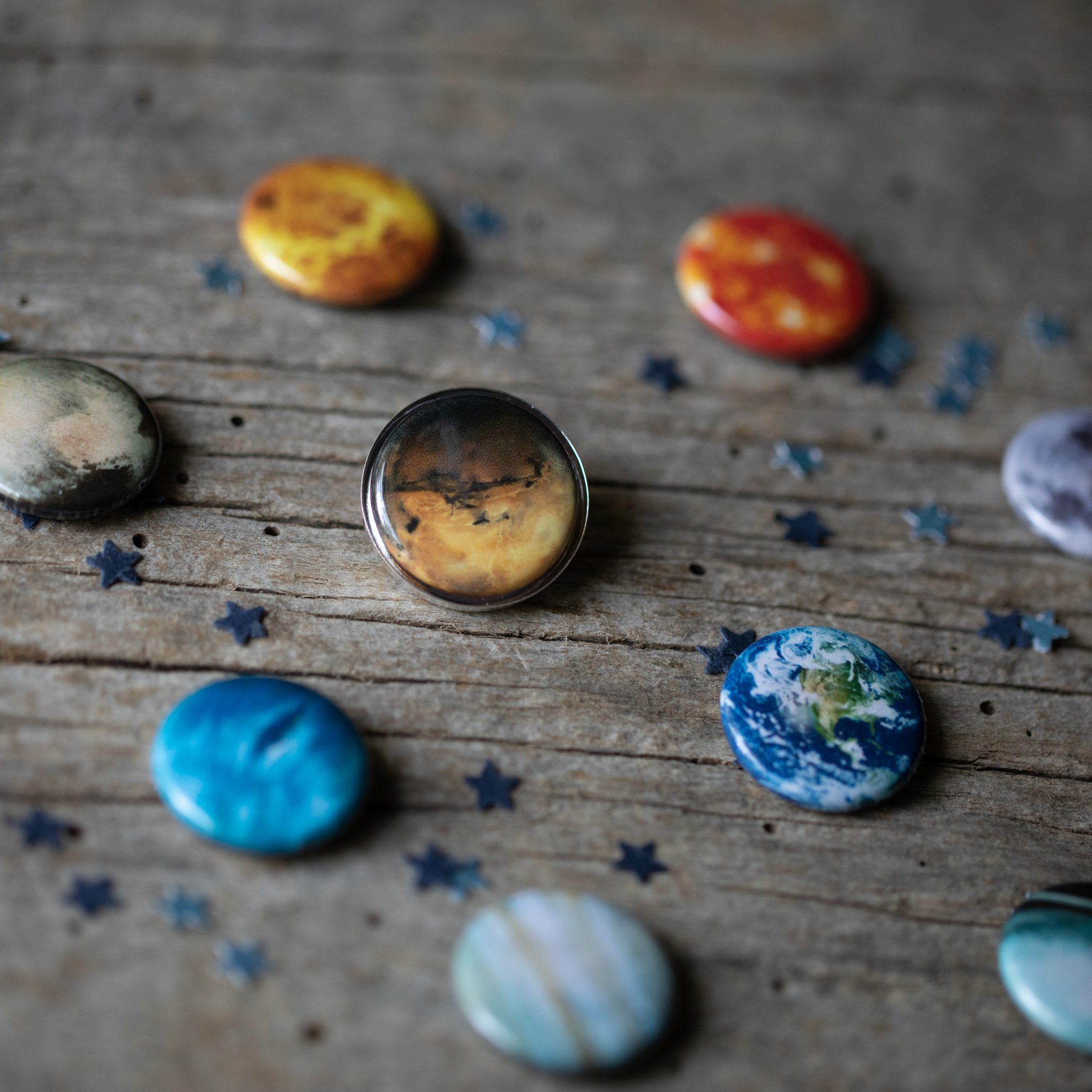 Interchangeable Solar System Lapel Pin featuring 10 images of planets, the Sun, and the Moon in silver and bronze tones.