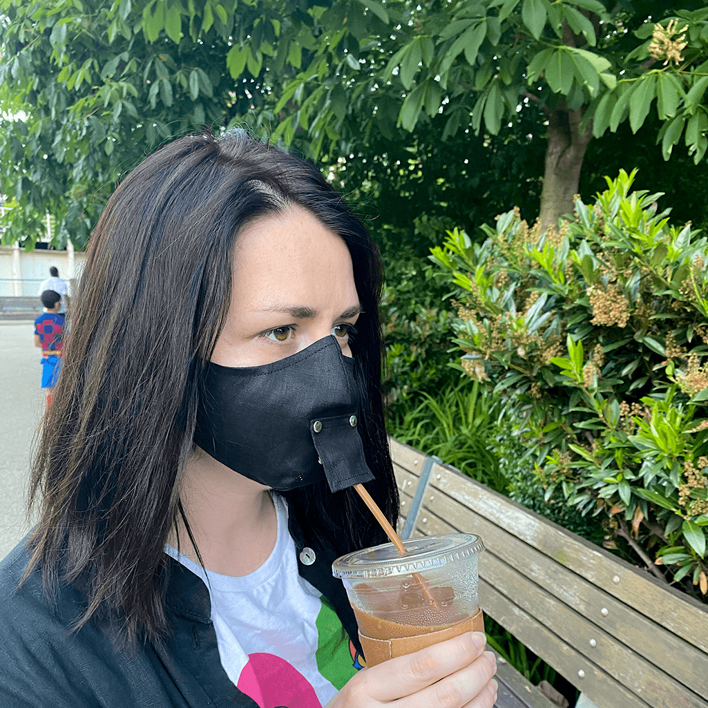 A stylish black face mask made from 100% organic linen, featuring a straw hole for easy sipping, adjustable elastic loops, and a moldable nose bridge.