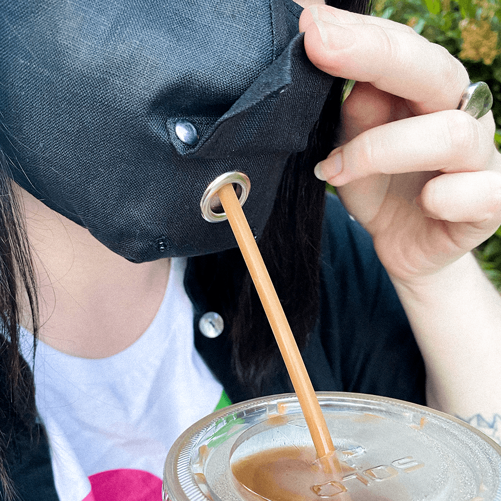 A stylish black face mask made from 100% organic linen, featuring a straw hole for easy sipping, adjustable elastic loops, and a moldable nose bridge.